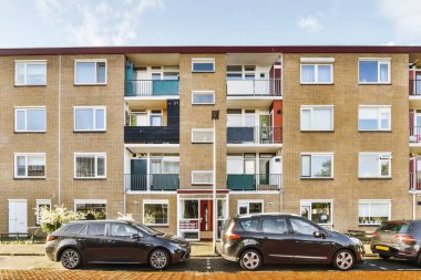 İki araba çok katlı bir apartmanın önüne park edilmiş. Çatısı ve pencereleri baltalı.