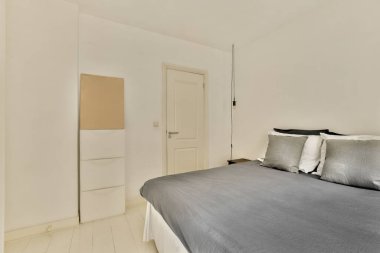 Beyaz duvarları ve ahşap döşemeleri olan bir odada yatağın üstünde asılı bir ayna var.