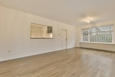 Ahşap döşemeleri ve beyaz duvarları olan boş bir oturma odası, üzerinde bir ayna var.