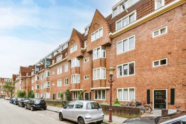 Amsterdam, Hollanda - 10 Nisan 2021: Beyaz pencereli ve kapılı bazı kırmızı tuğlalı binaların önünde cadde kenarına park edilmiş çok sayıda araba