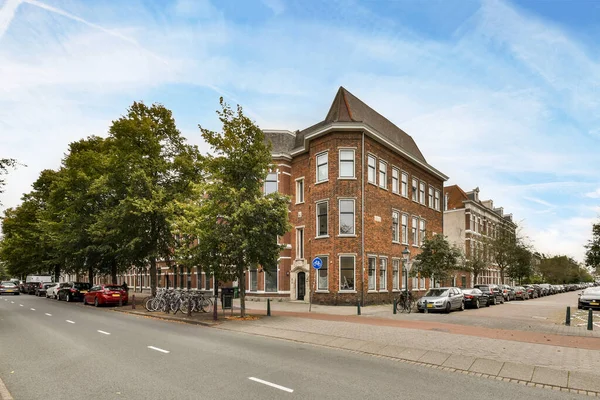 アムステルダム オランダ 2021 古い赤レンガのアパートの建物の前の縁石や木に駐車車のある街の通り — ストック写真
