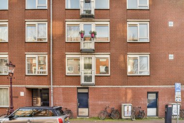 Amsterdam, Hollanda - 10 Nisan 2021: Önünde bisikletleri olan bir apartman ve yan yana park edilmiş iki araba.