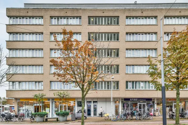 Amsterdam, Hollanda - 10 Nisan 2021: önünde bisikletleri park edilmiş bir apartman ve dışarıda arabalarına doğru yürüyen insanlar