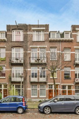 Amsterdam, Hollanda - 10 Nisan 2021: Tuğladan bir apartmanın önüne park edilmiş iki araba, camlarında balyalar ve ikinci kattaki camlar var.