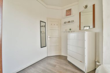 Beyaz duvarları ve köşesinde ahşap döşemeleri olan boş bir oda, duvarda bir ayna var.