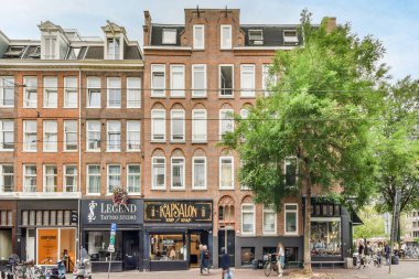 Amsterdam, Hollanda - 10 Nisan 2021: kaldırımda yürüyen insanların ve yanından geçen arabaların bulunduğu bir binanın önündeki bir ağaç