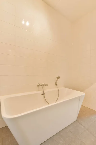 タイル張りの床と壁が描かれた浴室の角に白い浴槽があり — ストック写真