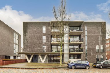 Güneşli bir günde, bir apartmanın önüne park edilmiş iki araba. Üzerinde mavi gökyüzü ve tüylü beyaz bulutlar var.