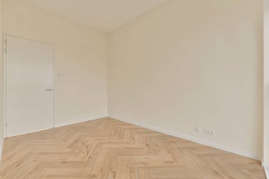 Beyaz duvarları ve sağ tarafında ahşap döşemeleri olan boş bir oda. Köşede solda bir kapı var.