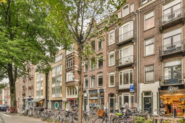 Amsterdam, Hollanda - 10 Nisan 2021: Birçok pencere ve balyası olan bir apartmanın önünde caddenin kenarına parketmiş bisikletler
