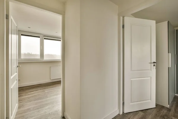 右边门上有一个有木制地板和白色装饰的空房间 是一个向外看的大窗户 — 图库照片