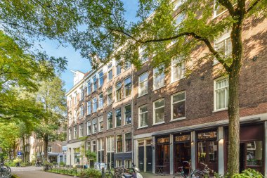 Amsterdam, Hollanda - 10 Nisan 2021: Bazı bisikletler uzun tuğlalı binaların önünde bir caddenin kenarına park ettiler.
