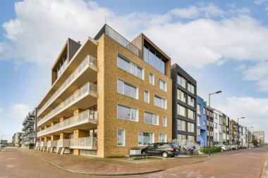 Amsterdam, Hollanda - 10 Nisan 2021: Bir apartman kompleksi. Arabalar caddenin kenarına park edilmiş bina önünde ve mavi gökyüzü yukarıda.