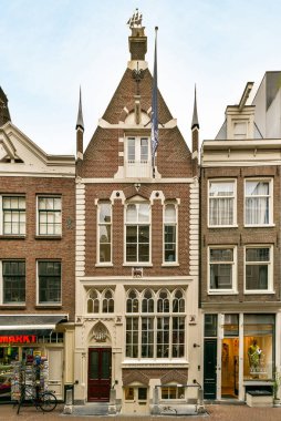 Amsterdam, Hollanda - 10 Nisan 2021: Tepesinde bir saat ve önünde bir bisiklet olan bir bina