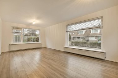 Boş bir oturma odası, ahşap döşeme ve evin önündeki sokağa bakan büyük pencereli.