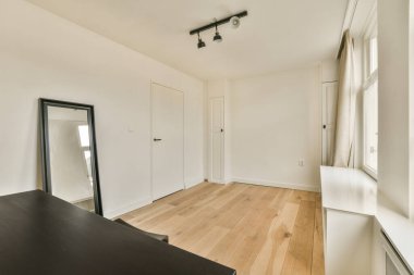 Beyaz duvarları ve sağ tarafında ahşap döşemeleri olan boş bir oda. Köşesinde bir ayna var.