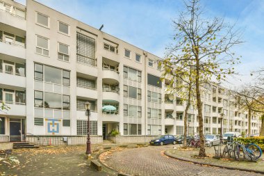 Kaldırımda bisikletleri olan bir apartman dairesi ve otoparkta yan yana park edilmiş arabalar.