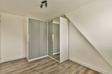 Beyaz duvarları ve ahşap döşemeleri olan boş bir oda. Köşedeki duvarda bir ayna var.