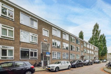 Amsterdam, Hollanda - 10 Nisan 2021: Bazı arabalar beyaz pencereli tuğla apartmanların önüne park etmiş.