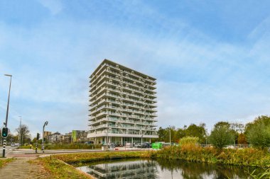 Amsterdam, Hollanda - 10 Nisan 2021: Köprünün önündeki nehir kıyısında bir apartman ve üzerinde arabalar park edilmiş binalar