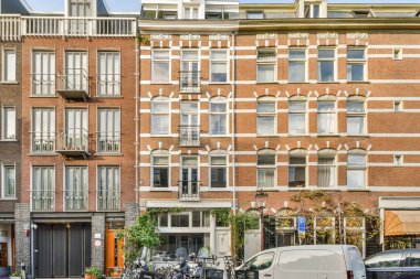 Amsterdam, Hollanda - 10 Nisan 2021: Kenarında arabalar olan bir şehir caddesi ve arkalarında binaların önünde yürüyen insanlar