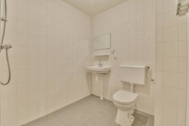 Duvarlarında ve zemininde beyaz fayanslar olan küçük bir banyo ve odanın köşesinde bir tuvalet.