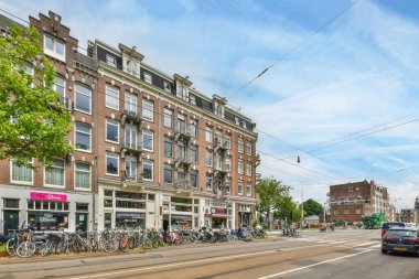 Amsterdam, Hollanda - 10 Nisan 2021: Yolun kenarına park edilmiş uzun tuğlalı binaların önünde arabaları ve bisikletleri olan bir sokak