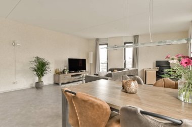 Oturma odası, yemek masası ve kanepelerin önünde sandalyeler duvarda büyük bir ayna var.