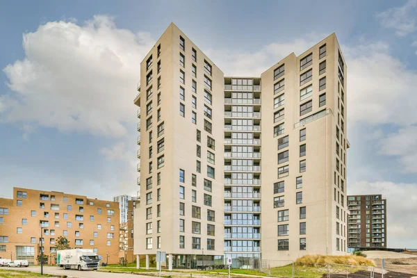 Şehir merkezinin ortasında büyük bir apartman binası. Sokakta arabaları park edilmiş ve insanlar etrafta dolaşıyor.