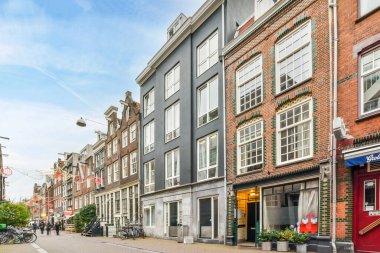 Amsterdam, Hollanda - 10 Nisan 2021: Yol kenarındaki ara sokaklara park edilmiş binalar ve bisikletlerle dolu bir şehir caddesi