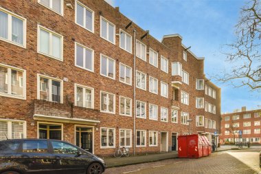 Beyaz pencereli ve kepenkli kapısı olan tuğladan bir binanın önüne park etmiş bir araba.