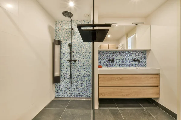 a bathroom with blue and white mosaic tiles on the walls, along with a wooden vanity in the shower is next to the sink