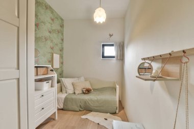 Bir yatak, şifonyer ve yanındaki duvarda ayna olan küçük bir oda yeşil bir çiçek duvar kağıdıdır.