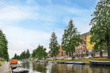 Amsterdam, Hollanda - 10 Nisan 2021: Nehrin diğer yakasındaki bazı tekneler ve arkasında ağaçlar olan binalar