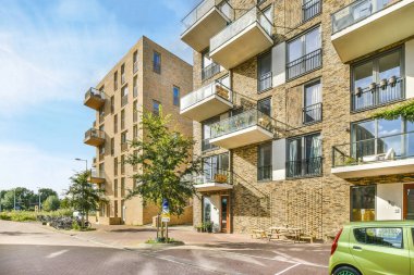 Güneşli bir günde, bir apartmanın önüne park edilmiş yeşil bir araba. Mavi gökyüzü ve pencerelerinden güneş ışığı görünüyor.