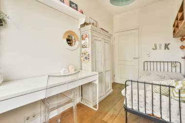 Yatağın yanındaki duvarda yatağı, masası ve aynası olan bir çocuk odası beyazdır.