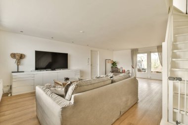 Odanın ortasında beyaz duvarları ve ahşap döşemeleri olan bir oturma odası duvarda büyük bir düz ekran televizyon var.