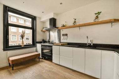 Üzerinde siyah tezgah ve beyaz dolaplar olan bir mutfak. Yukarıda lavabonun önünde oturan bir bank var.