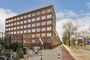 Şehrin caddesindeki tuğla bir binanın önüne park edilmiş bir bisiklet. Girişin etrafında ağaçlar ve çalılar var.