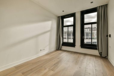 Ahşap döşemeli boş bir oda ve fotoğraftaki iki büyük pencere içeriden dışarıya bakıyor.