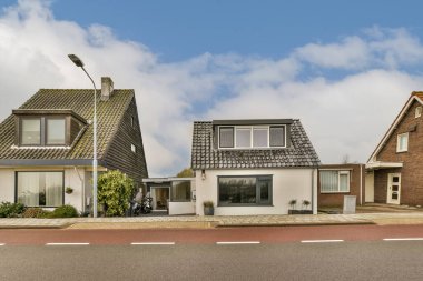 Yolun kenarındaki bazı evler mavi gökyüzü ve beyaz bulutlar sokağın karşısından çekiliyor.