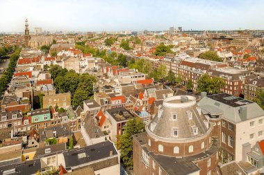 Amsterdam, Hollanda - 10 Nisan 2021: Binanın tepesinden arka plandaki bazı bina ve ağaçlara bakan bir şehir mavi gökyüzü