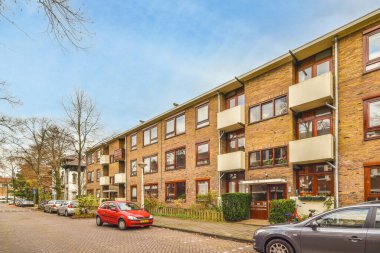 Amsterdam, Hollanda - 10 Nisan 2021: Birçok penceresi olan tuğladan apartmanların önüne park edilmiş bazı arabalar