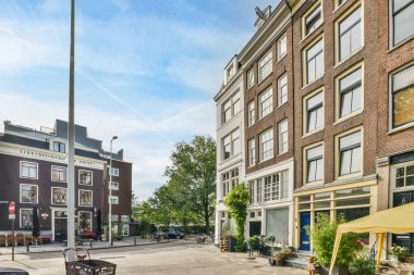 Masaları ve şemsiyeleri olan, uzun kahverengi tuğlalı binalarla çevrili bir alan.