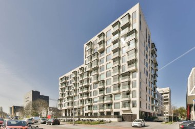 Amsterdam, Hollanda - 10 Nisan 2021: Kenarında arabalar ve fotoğrafın ortasındaki binalar olan bir şehir caddesi açık mavi gökyüzü