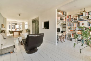 Arkasında beyaz ahşap döşeme ve kitaplıklarla dolu büyük bir kitaplık olan oturma odası.