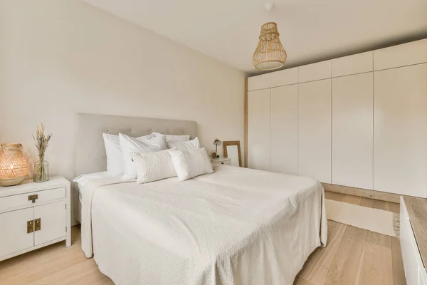 ベッドの横の壁にベッドと白い食器棚のある寝室にはベッドの上にランプがあります — ストック写真