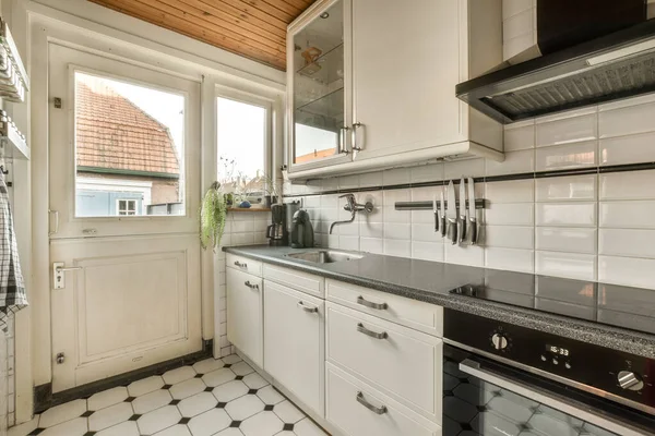 a kitchen with black and white tiles on the floor, along with an open door that leads to a patio
