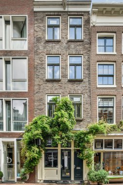 Amsterdam, Hollanda - 10 Nisan 2021: Dışında birçok pencere ve bitki büyüyen bir bina, önünde girişte park etmiş bir bisiklet var