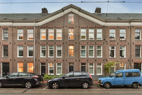 オランダ アムステルダム 2021年4月10日 レンガ造りの建物の前に2両の車が停車し 両側に多くの窓があり 隣に1両の車が停まっている — ストック写真